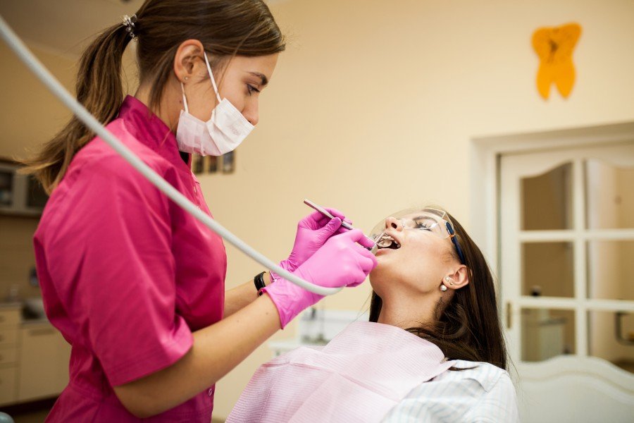 Dentist in pink scrubs and gloves examining a patient’s teeth during a dental procedure.